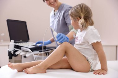 Sonograf, klinikte küçük kızın dizinin ultrason muayenesini yapıyor.