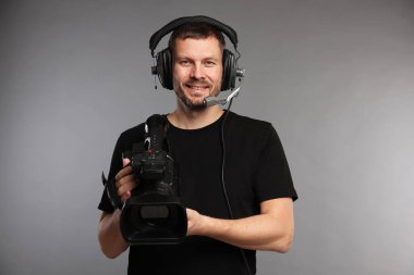 Profesyonel kameralı ve kulaklıklı bir adam gri arka planda.