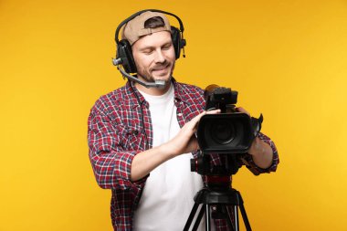 Profesyonel kamera ve turuncu arka planda kulaklığı olan bir adam.