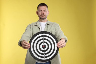 Hedef alınıyor. Sarı arka planda dart tahtası olan adam.