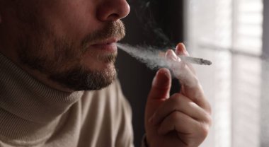 Pencerenin yanında sigara içen adam, yakın plan.