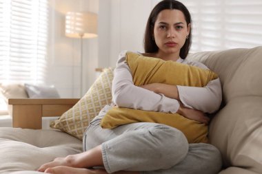 Depresyondaki kadın evdeki kanepede yastığa sarılıyor.