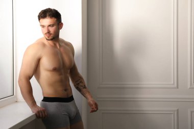 Beyaz duvarın yanındaki açık gri iç çamaşırlı genç adam. Metin için boşluk