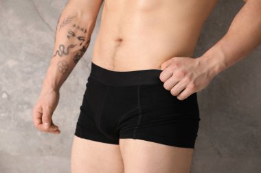 Gri duvarın yanında şık siyah iç çamaşırlı genç adam, yakın plan.