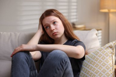 Evdeki kanepede oturan üzgün genç kız.