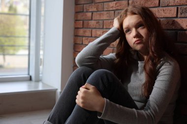 Evdeki tuğla duvarın yanındaki üzgün genç kız.