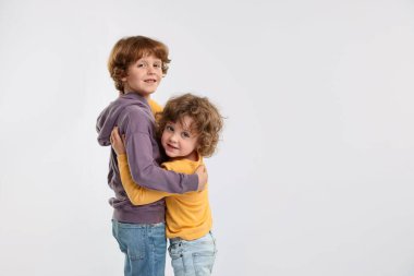 Beyaz arka planda kucaklaşan sevimli küçük kardeşler.