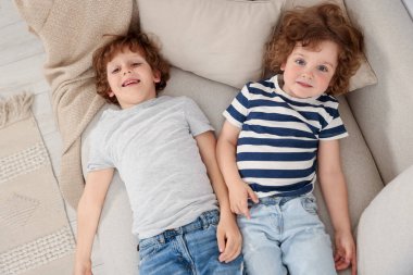 Sevimli küçük kardeşler birlikte kanepede yatıyorlar, manzaranın üstünde.