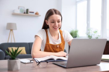 Evde dizüstü bilgisayarla ödev yapan genç bir kız.