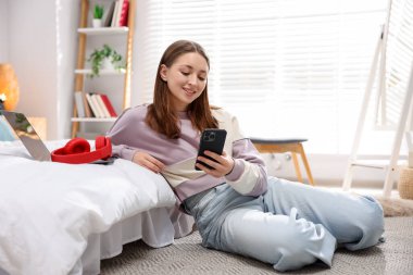 Genç kız evde yerde akıllı telefon kullanıyor.