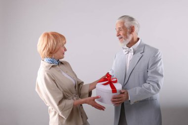 Açık gri arka planda hediye kutusu olan sevimli yaşlı çift.