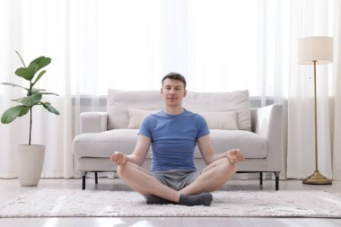 Genç adam evde yerde yoga yapıyor.