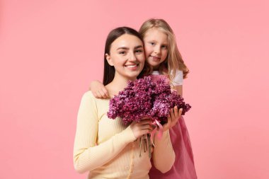 Anne ve kızı pembe arka planda bir demet leylak çiçeğiyle