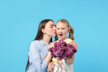 Anne ve kızı açık mavi arka planda bir demet leylak çiçeğiyle