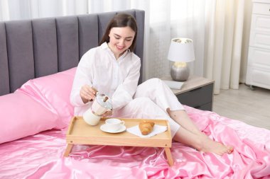 Gülümseyen kadın kahve dolduruyor Moka çaydanlığından yatağa pembe ipek çarşaflarla.