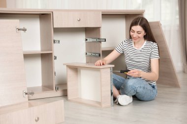 Gülümseyen kadın evde yerde tornavidayla mobilya monte ediyor.