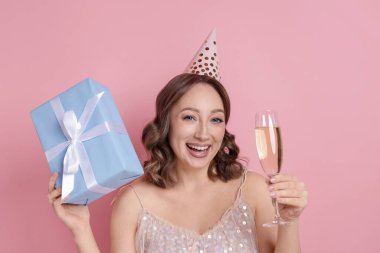 Doğum günü kutlaması. Bir bardak köpüklü şarap ve pembe arka planda bir hediye.