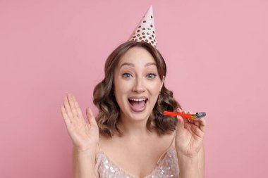 Doğum günü kutlaması. Pembe arka planda parti kornası çalan kadın.