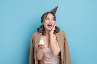 Doğum günü kutlaması. Açık mavi arka planda kek yiyen kadın.