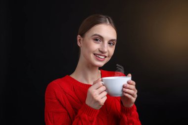 Kahverengi arka planda bir fincan kahveyle gülümseyen kadın.