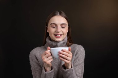 Kahverengi arka planda bir fincan kahveyle gülümseyen kadın.