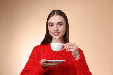 Bej renkli arka planda bir fincan kahveyle gülümseyen kadın