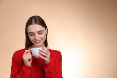 Bej renkli arka planda bir fincan kahveyle gülümseyen kadın. Metin için boşluk