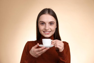 Bej renkli arka planda bir fincan kahveyle gülümseyen kadın