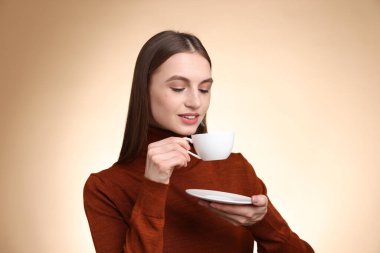 Bej renkli arka planda fincandan kahve içen kadın