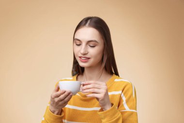 Bej renkli arka planda bir fincan kahveyle gülümseyen kadın