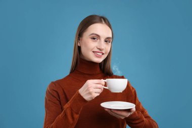 Açık mavi arka planda bir fincan kahveyle gülümseyen kadın.