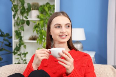 Evdeki kanepede bir fincan kahveyle gülümseyen kadın.