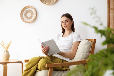 Evdeki rahat koltukta kitap okuyan güzel bir kadın.