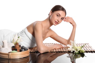 Beyaz arka planda bambu hasırında poz veren güzel bir kadın. Ayna yüzeyinde kaplıca ürünleri ve çiçekler