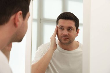 Yakışıklı adam aynada kendine bakıyor.