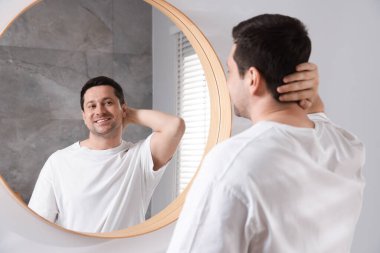 Yakışıklı adam aynada kendine bakıyor.