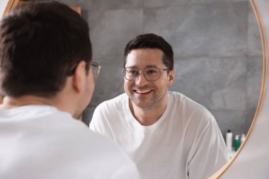 Yakışıklı adam aynada kendine bakıyor.