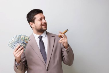 Dolar banknotları olan açgözlü bankacı gri arka planda puro içiyor. Metin için boşluk