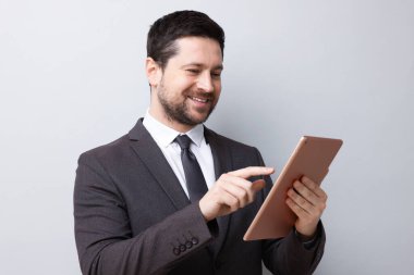 Gülümseyen işadamı açık gri arkaplanda tablet kullanıyor