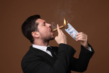 Açgözlü bankacı, kahverengi arka planda dolar banknotuyla puro yakıyor.