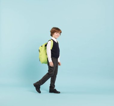 Açık mavi arka planda sırt çantası olan sevimli bir okul çocuğu.