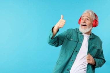 Kulaklıklı yaşlı adam açık mavi arkaplanda baş parmak gösteriyor, mesaj için boşluk