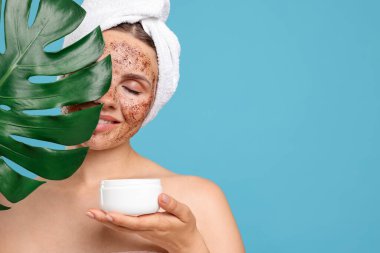 Yüzünde vücut fırçası, kavanoz ve canavar yaprağı açık mavi arka planda olan gülümseyen kadın. Metin için boşluk