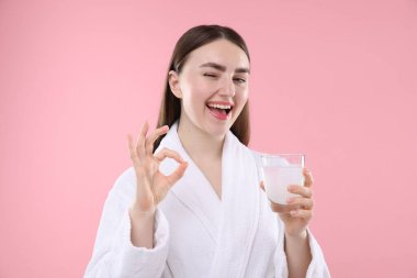 Bir bardak kolajen suyu olan mutlu kadın pembe arka planda iyi bir jest gösteriyor.