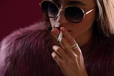 Kürk ceketli güzel bir kadın koyu pembe arka planda sigara içiyor, yakın plan.