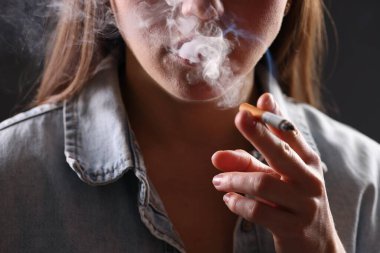 Arka planda sigara içen tişörtlü bir kadın, yakın plan. Kötü alışkanlık.
