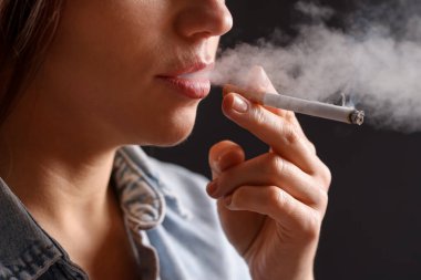 Arka planda sigara içen tişörtlü bir kadın, yakın plan. Kötü alışkanlık.