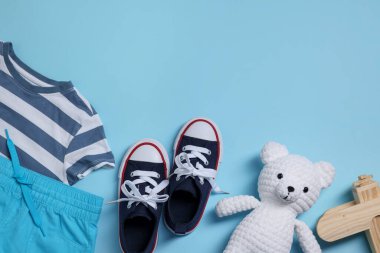 Oyuncak ayı, tahta oyuncak uçak, ayakkabılar ve açık mavi arka planda t-shirt, düz yatış. Metin için boşluk