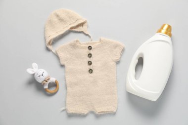 Bir şişe yumuşatıcı, oyuncak ve bebek kıyafetleri açık gri arka planda, düz yatıyordu.