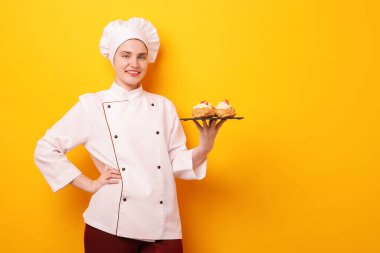 Üniformalı şekerlemeci turuncu arka planda lezzetli profiteroller tutuyor, mesaj için yer var.